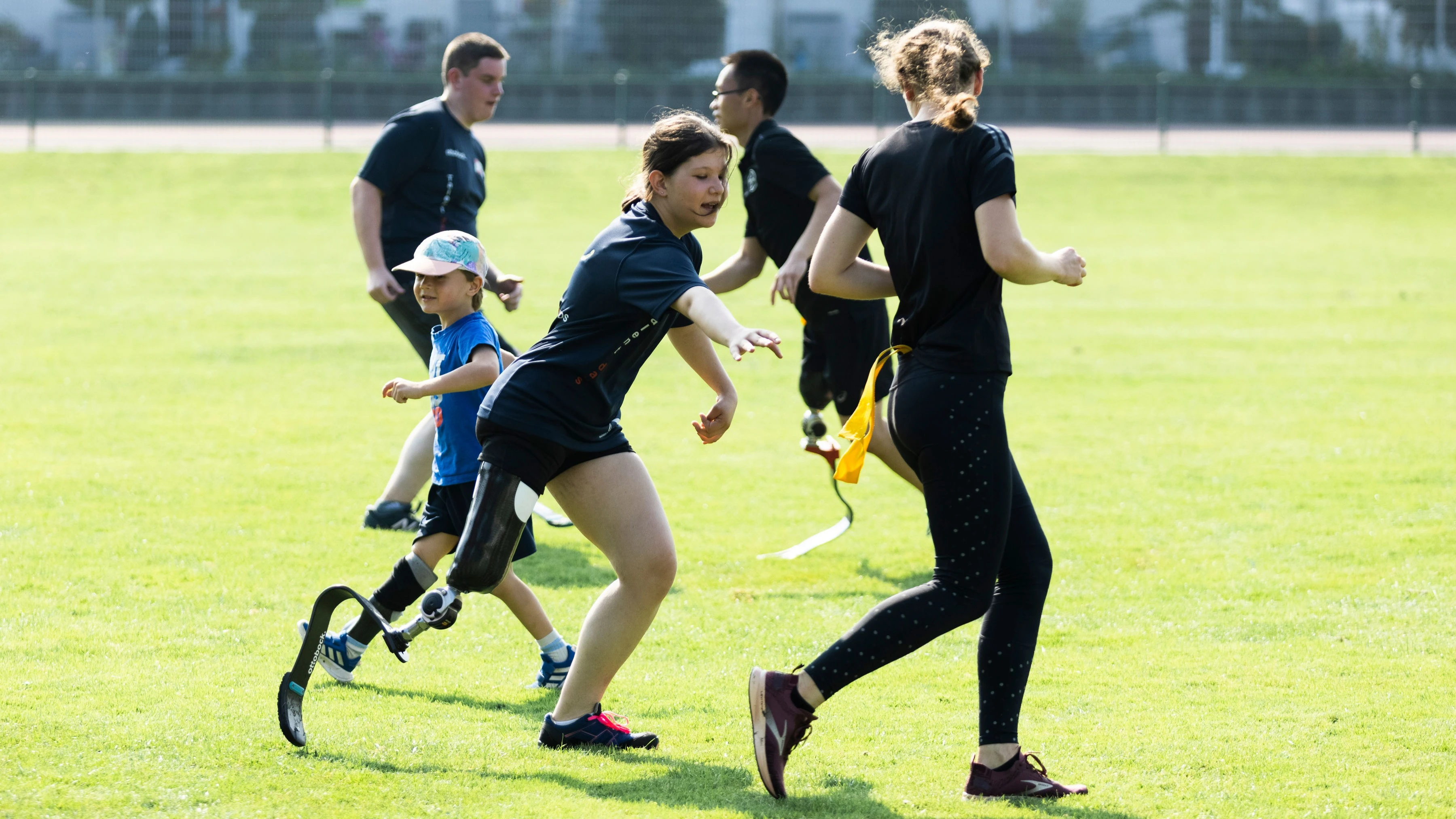 A group of kids playing outdoors games in a field. Some are wearing sports running prosthetic blades