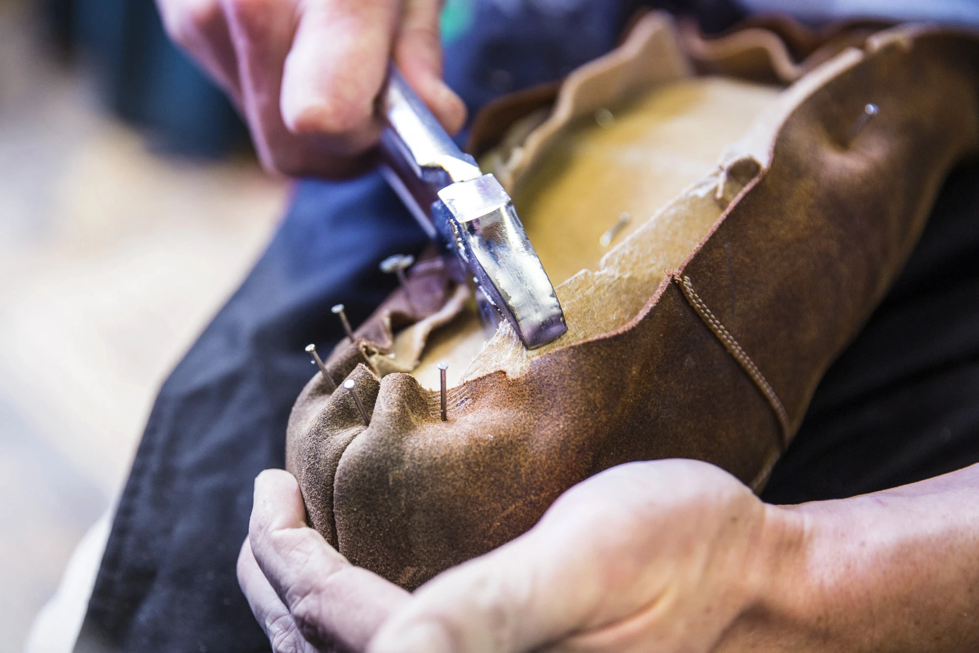 Hands working with tools on leather material, possibly crafting or repairing an item.