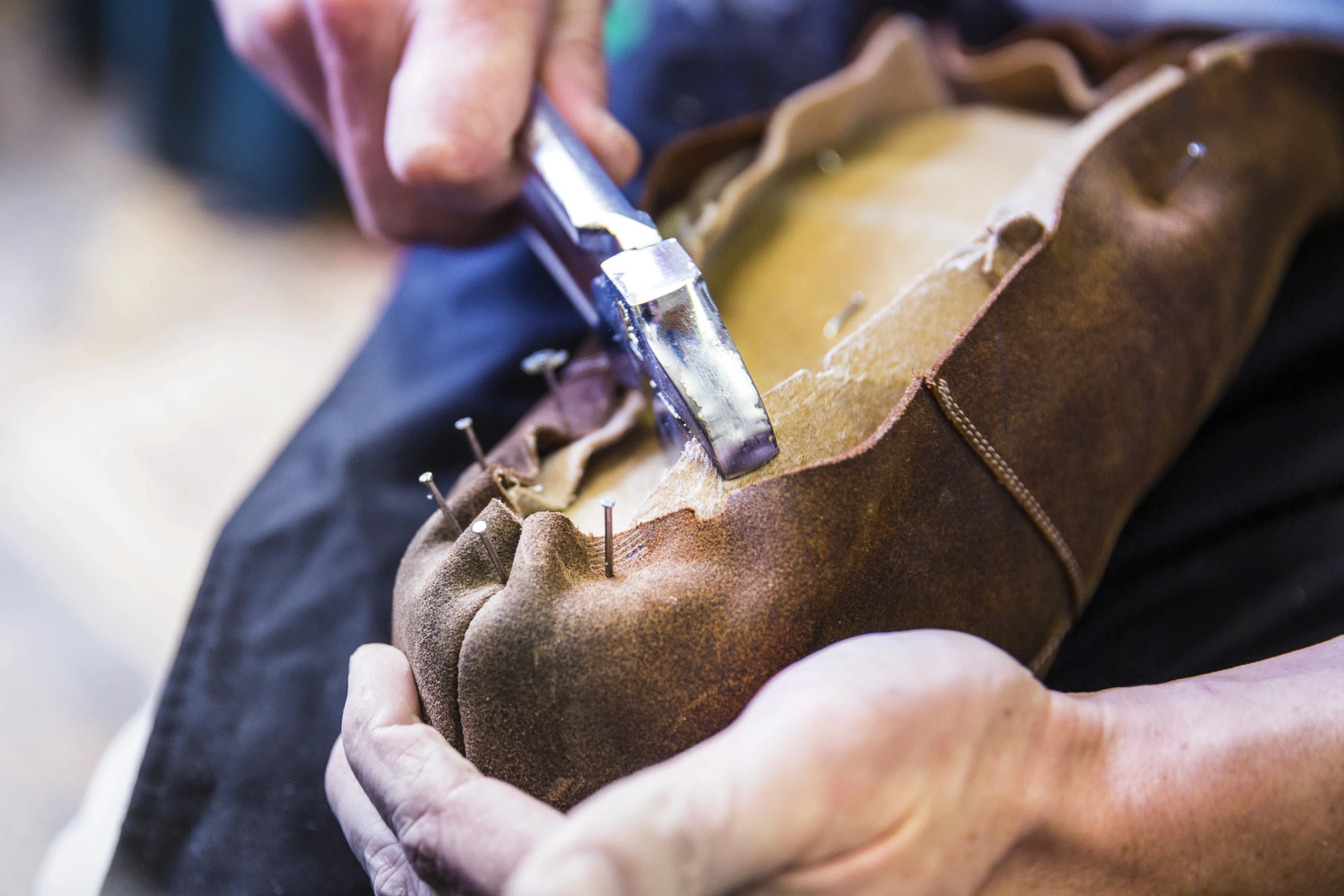 Hands working with tools on leather material, possibly crafting or repairing an item.