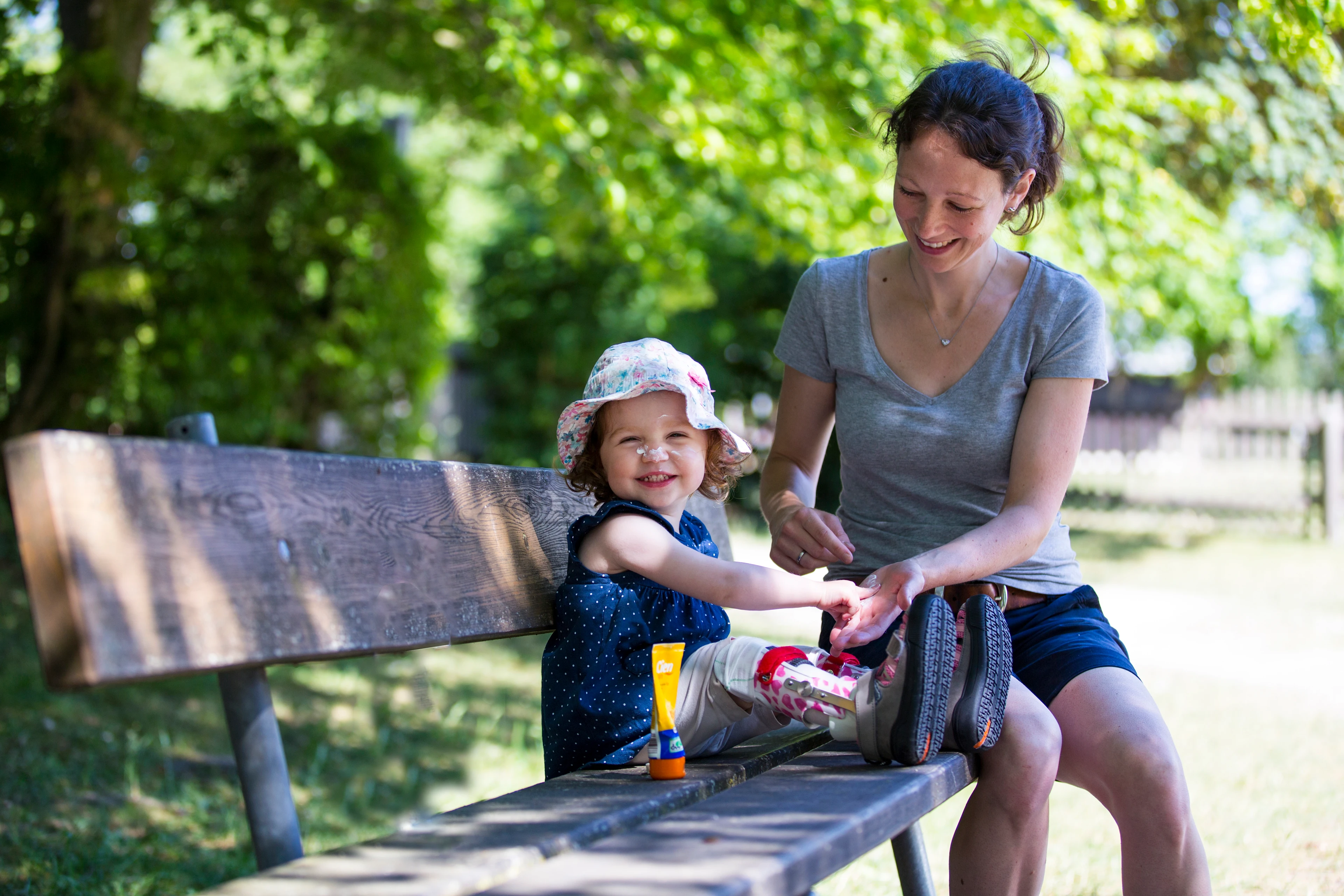 A young girl with foot braces sitting on a bench next to her mother.