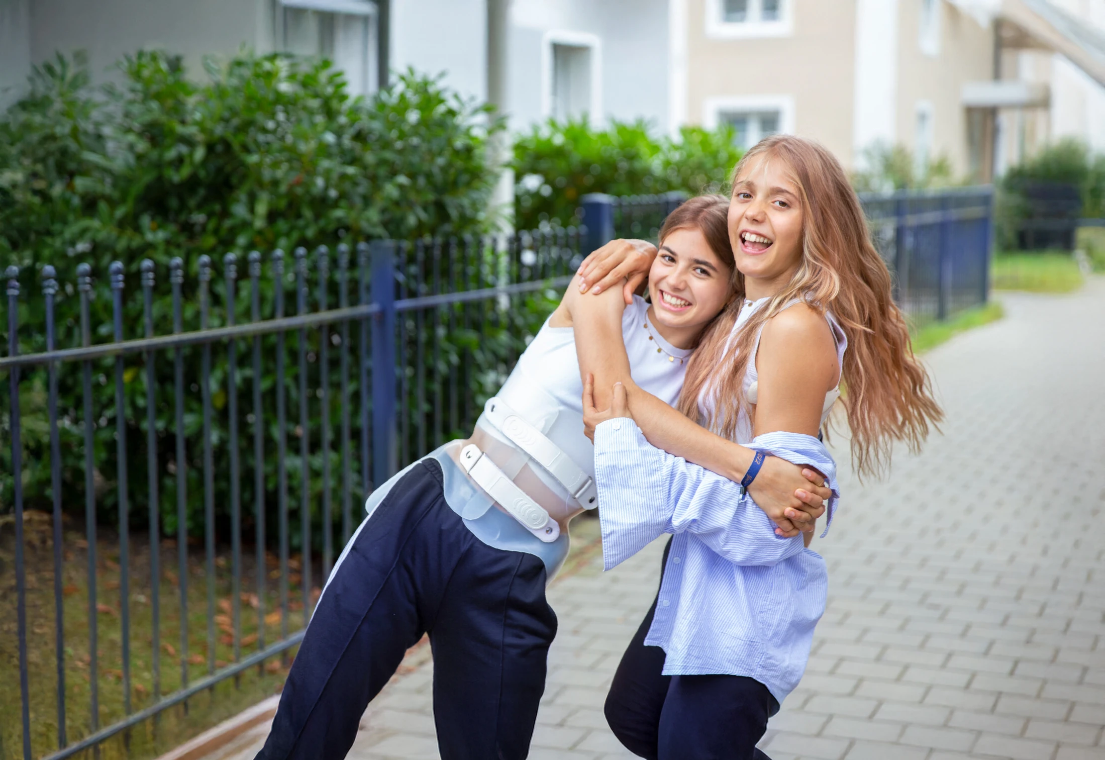 Two people standing outdoors and embracing; one is wearing a back brace.