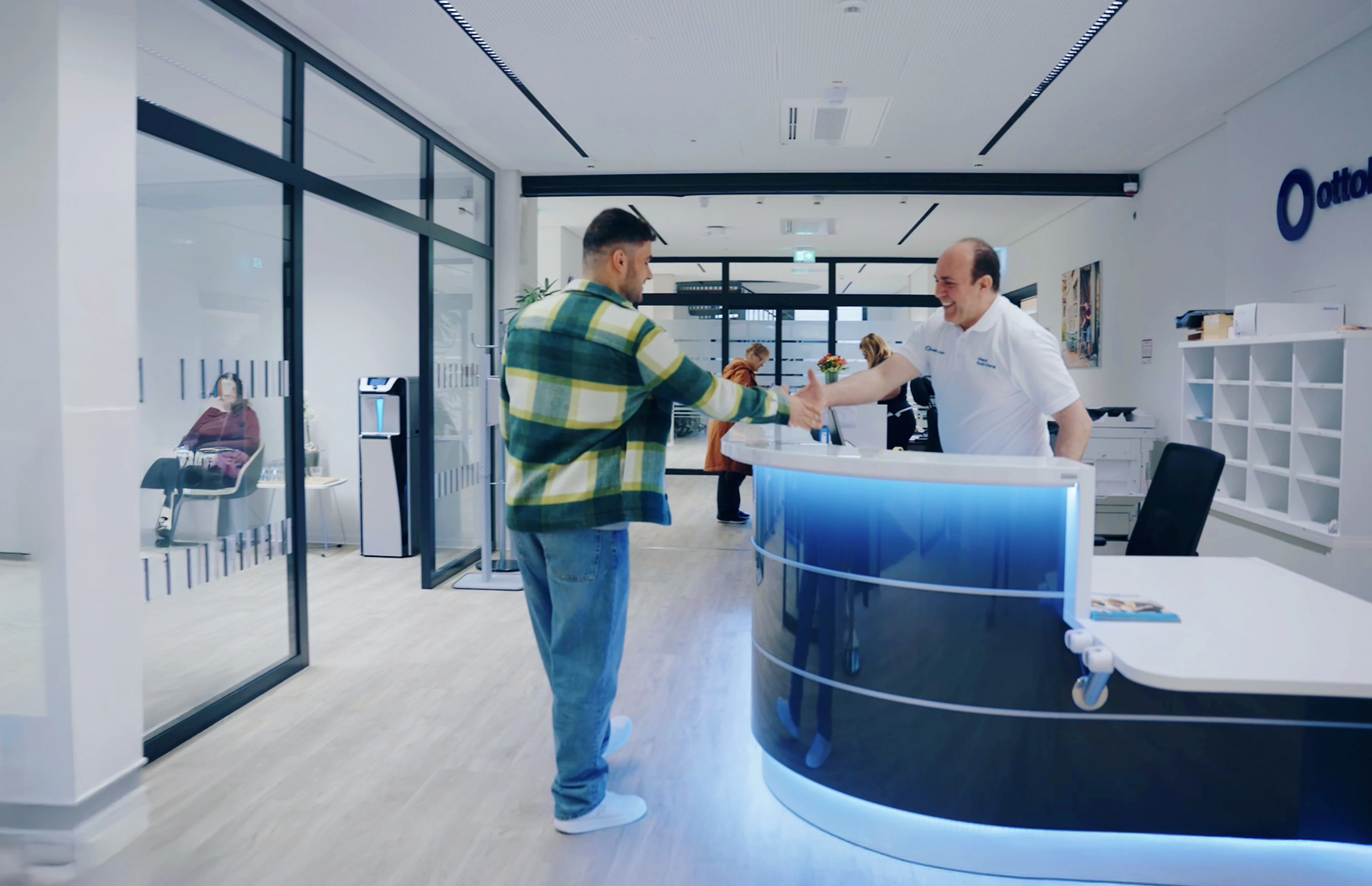 Two individuals shaking hands across a reception desk in an Ottobock clinic.