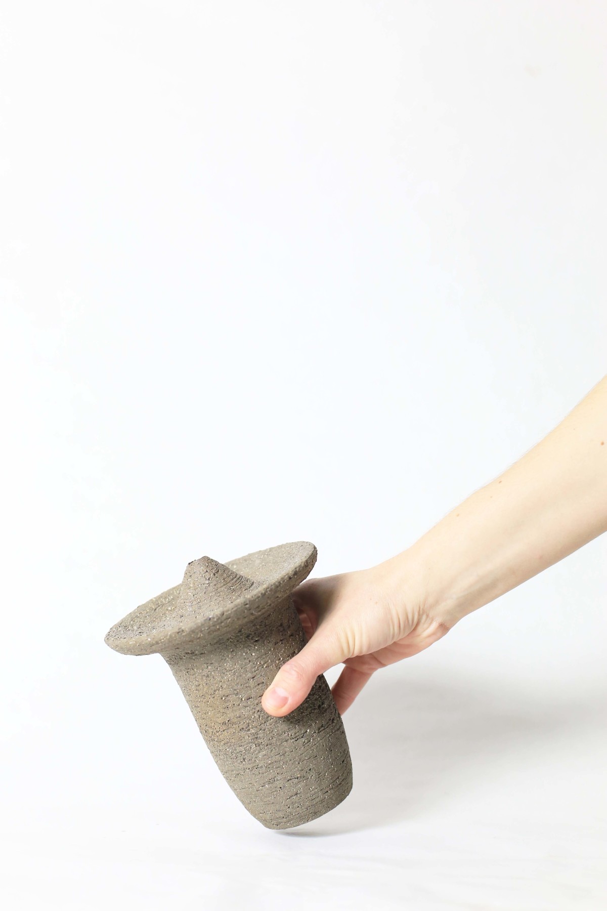 a hand holds Ufo shaped gray ceramic vase on a white background
