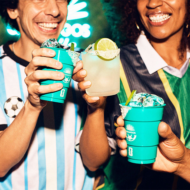 Friends in football jerseys toasting Casamigos Margaritas in commemorative cups.