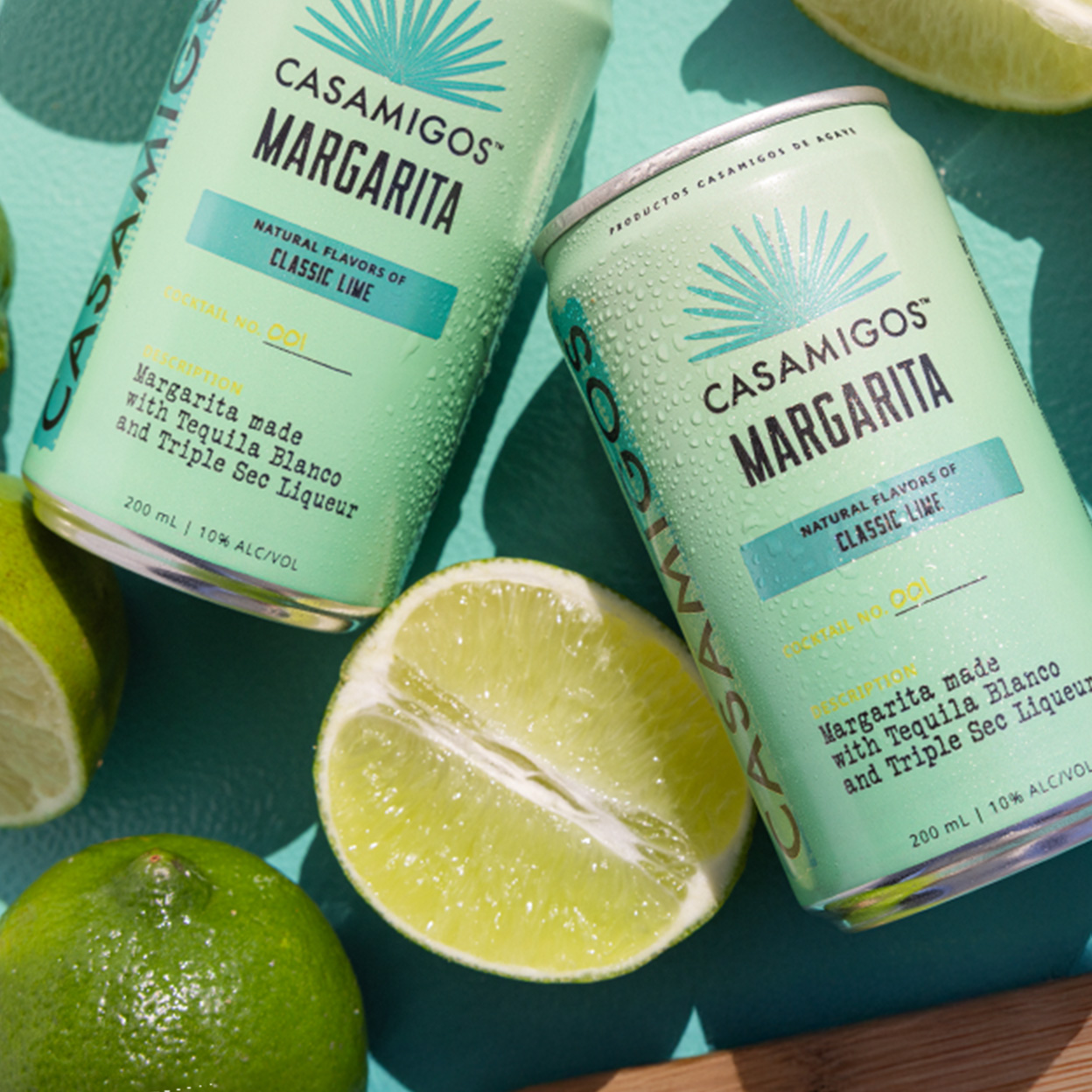 Two cans of Classic Lime Casamigos Margaritas surrounded by whole and halved limes.
