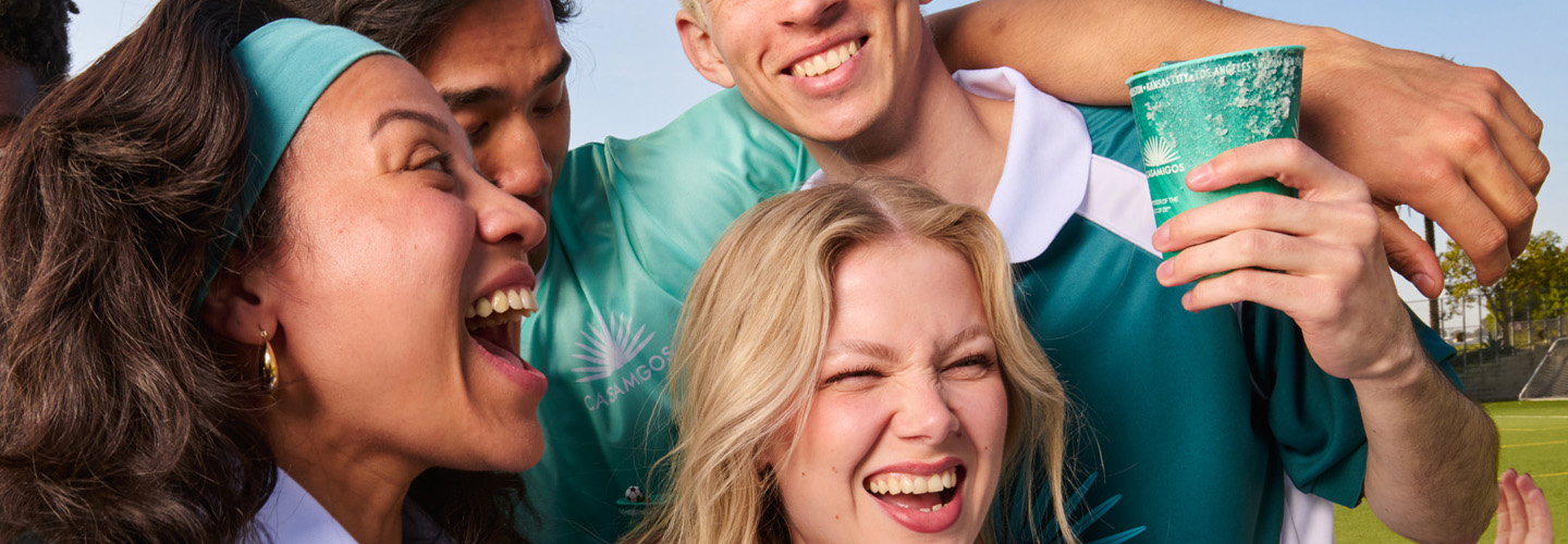 Close-up of friends smiling at a football match, one holding a Casamigos commemorative cup with a salted rim.