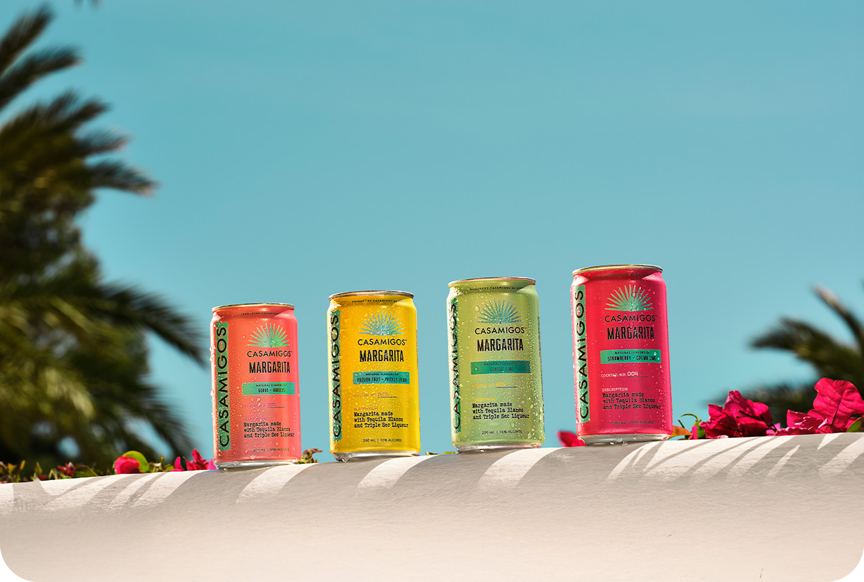 Casamigos Canned Margaritas on a ledge surrounded by pink flowers.