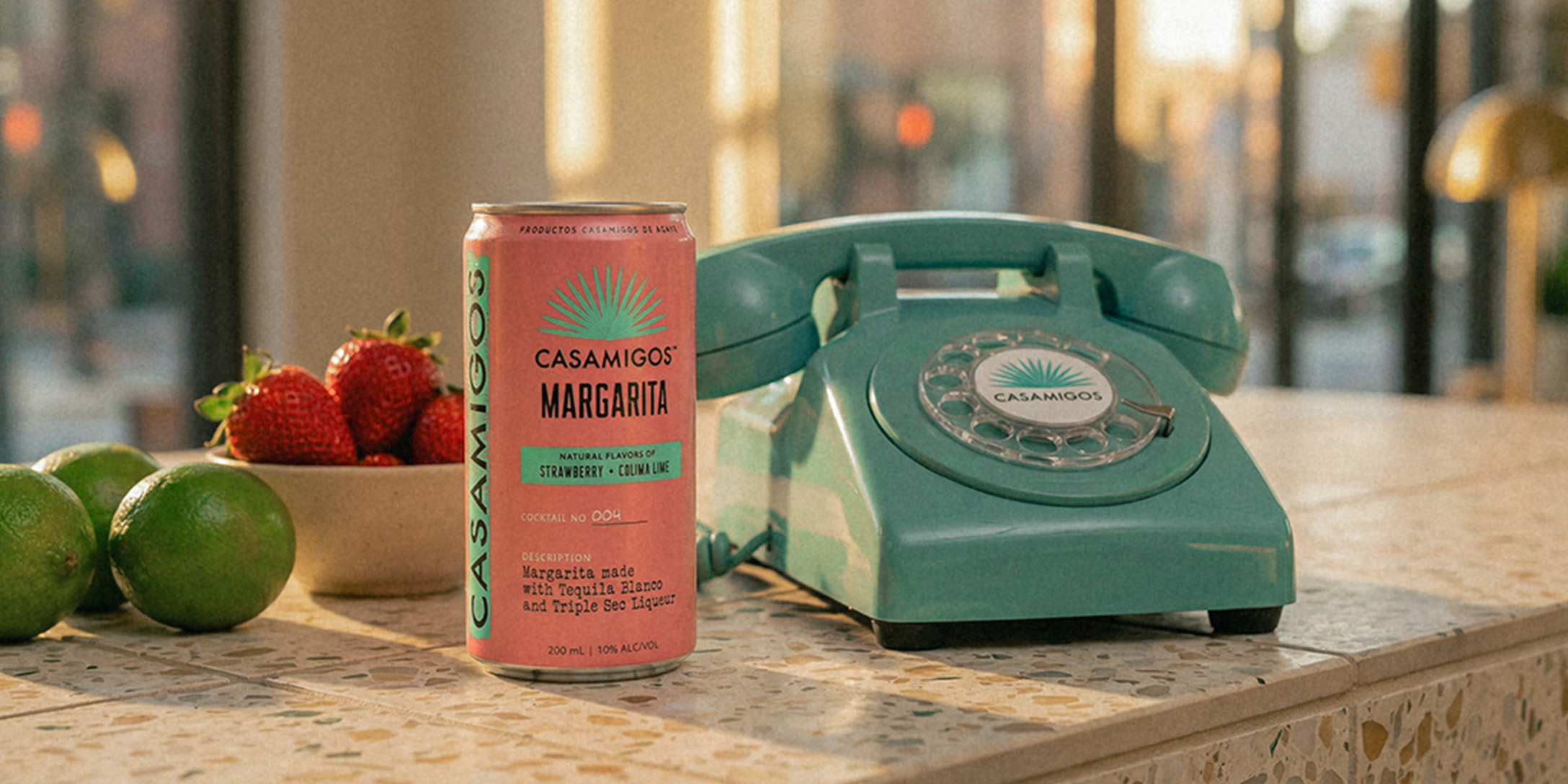 Teal rotary telephone on a countertop beside a can of Strawberry and Colima Lime Ready-To-Drink Casamigos Margarita, fresh strawberries, and whole limes
