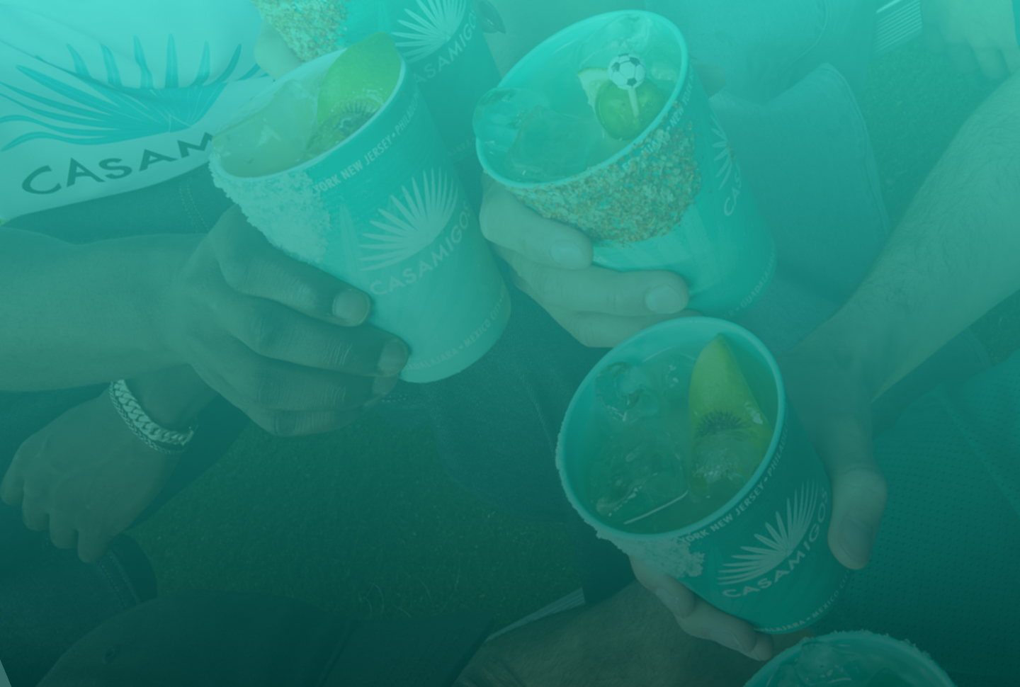 Three friends toasting with lime-garnished margaritas over ice in Casamigos branded cups, one featuring a festive mini soccer ball pick.