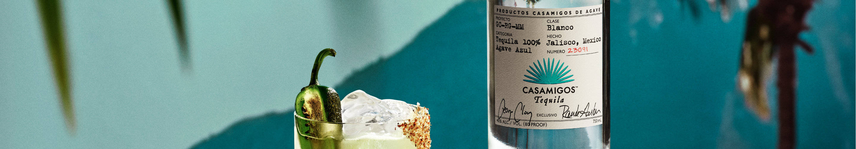 A Casamigos Spicy Margarita cocktail with half slice of jalapeno garnish next to a bottle of Casamigos Blanco tequila.