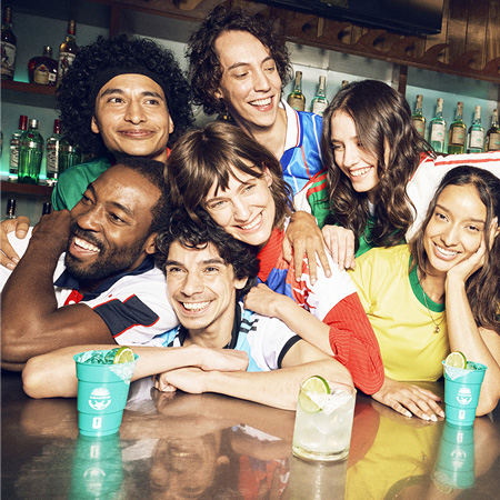 Friends in football jerseys gathered at a bar table, smiling and enjoying Casamigos Margaritas together during a watch party.
