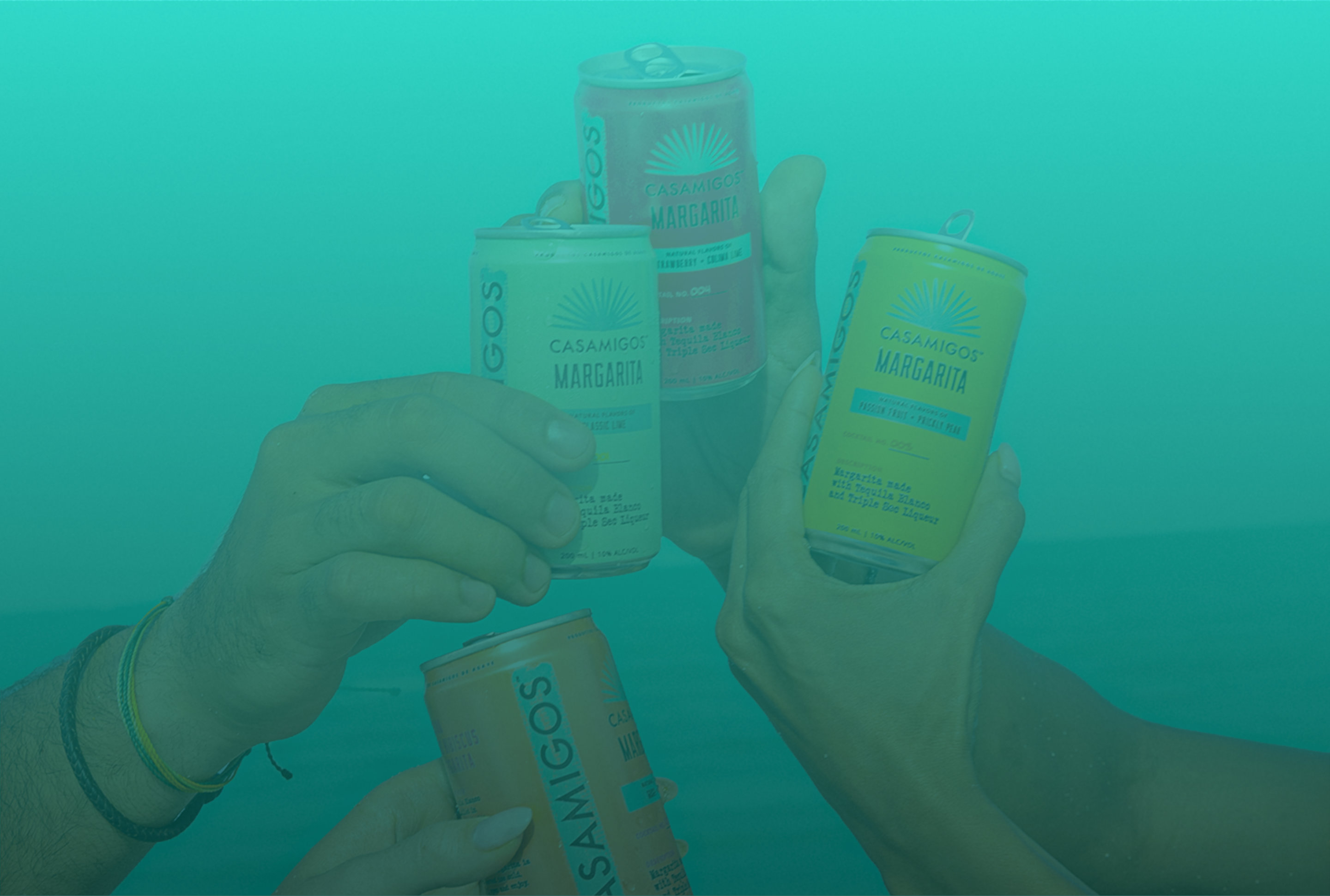 Four friends raising Ready-To-Drink Casamigos Margaritas cans in a toast with a teal ocean and sky in the background