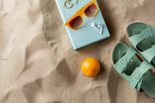 concepto de ocio y vacaciones de verano: zapatillas, naranjas, audífonos, reserva y gafas de sol en la arena de la playa