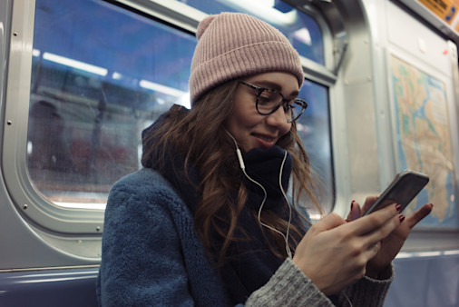 Portrait of a smiling pretty girl in earphones using mobile phone in subway train