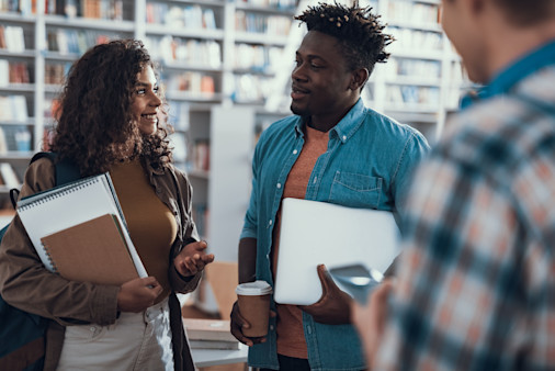 Friendly relaxed students standing in the library with their notes and smiling while enjoying their pleasant conversation