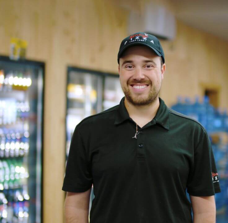 A happy Kenny's Pizza proprietor in a brightly lit shop.