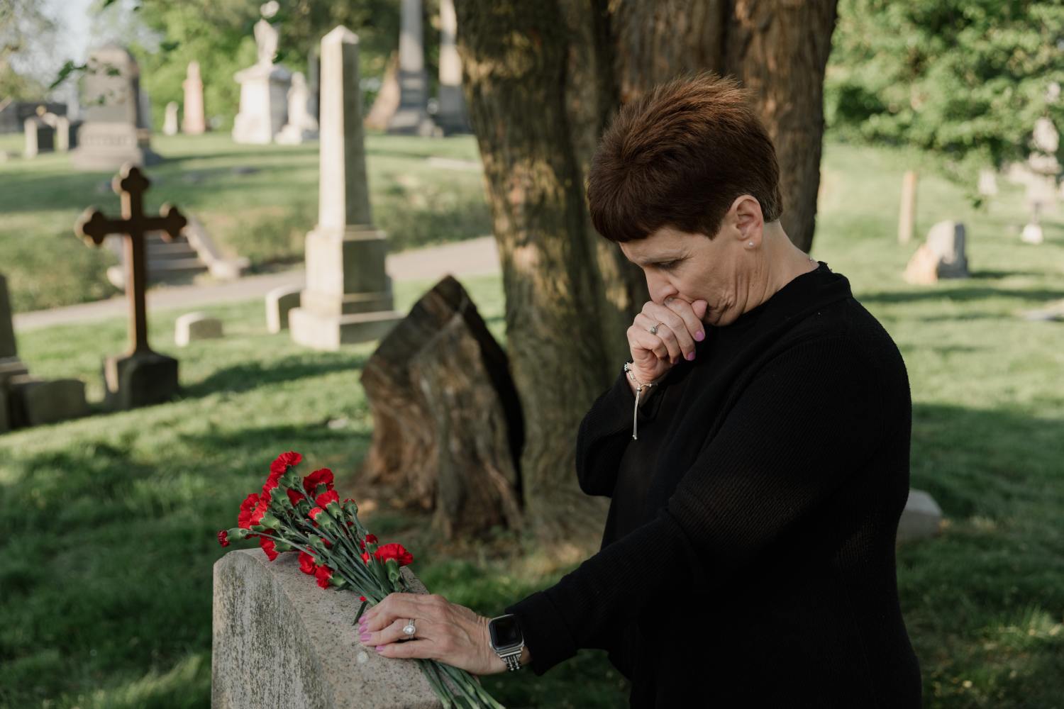 Woman at grave, thinking about responsibilities like how to claim life insurance benefits after death.
