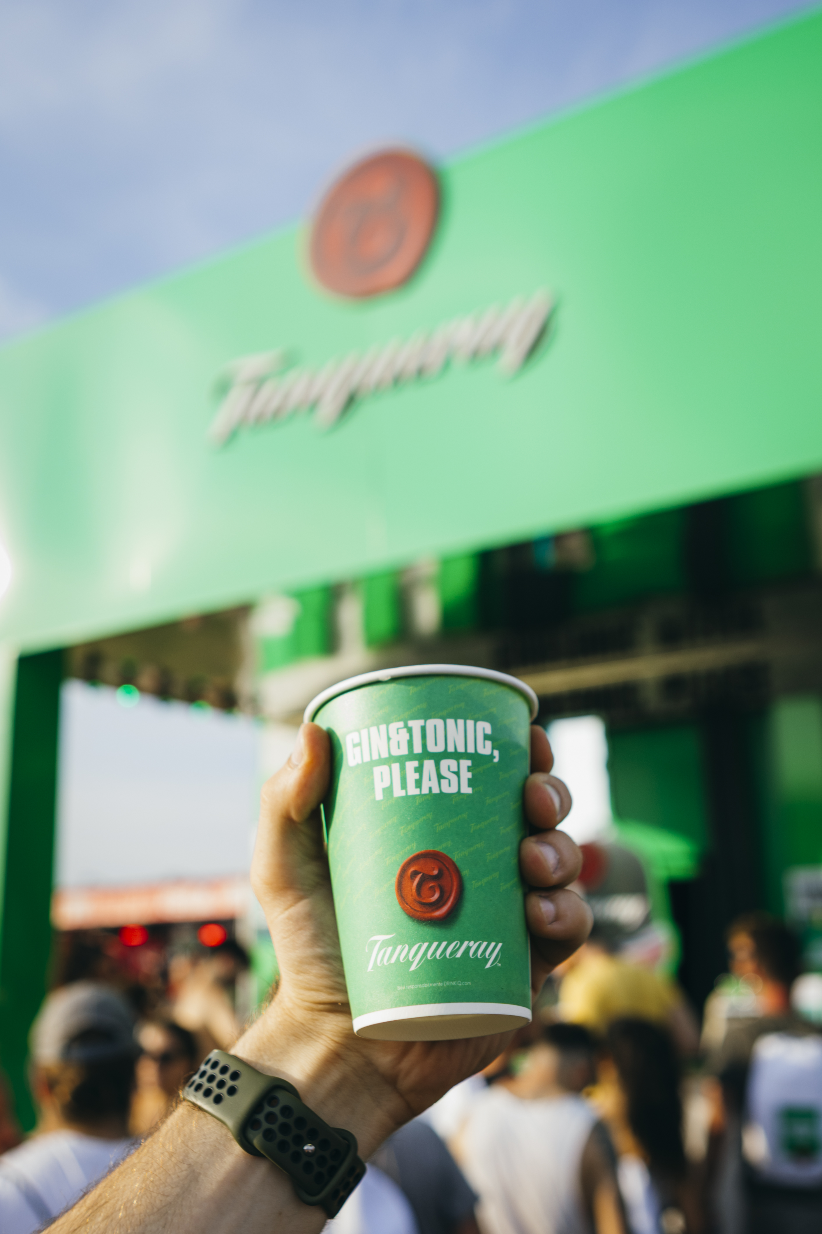 bicchiere verde con tanqueray tenuto in mano con lo stand tanqueray sullo sfondo
