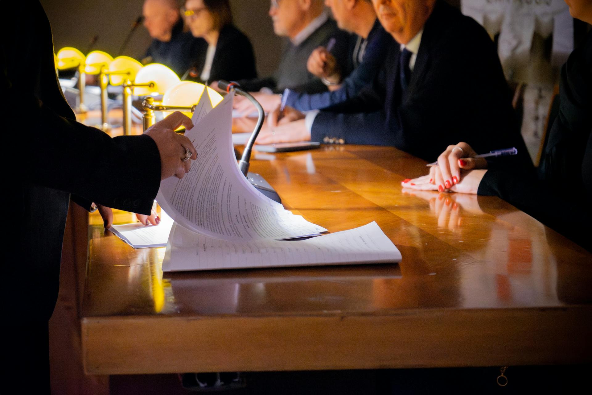 A close-up view of a business meeting, with one participant holding a document while others take notes at a polished wooden table