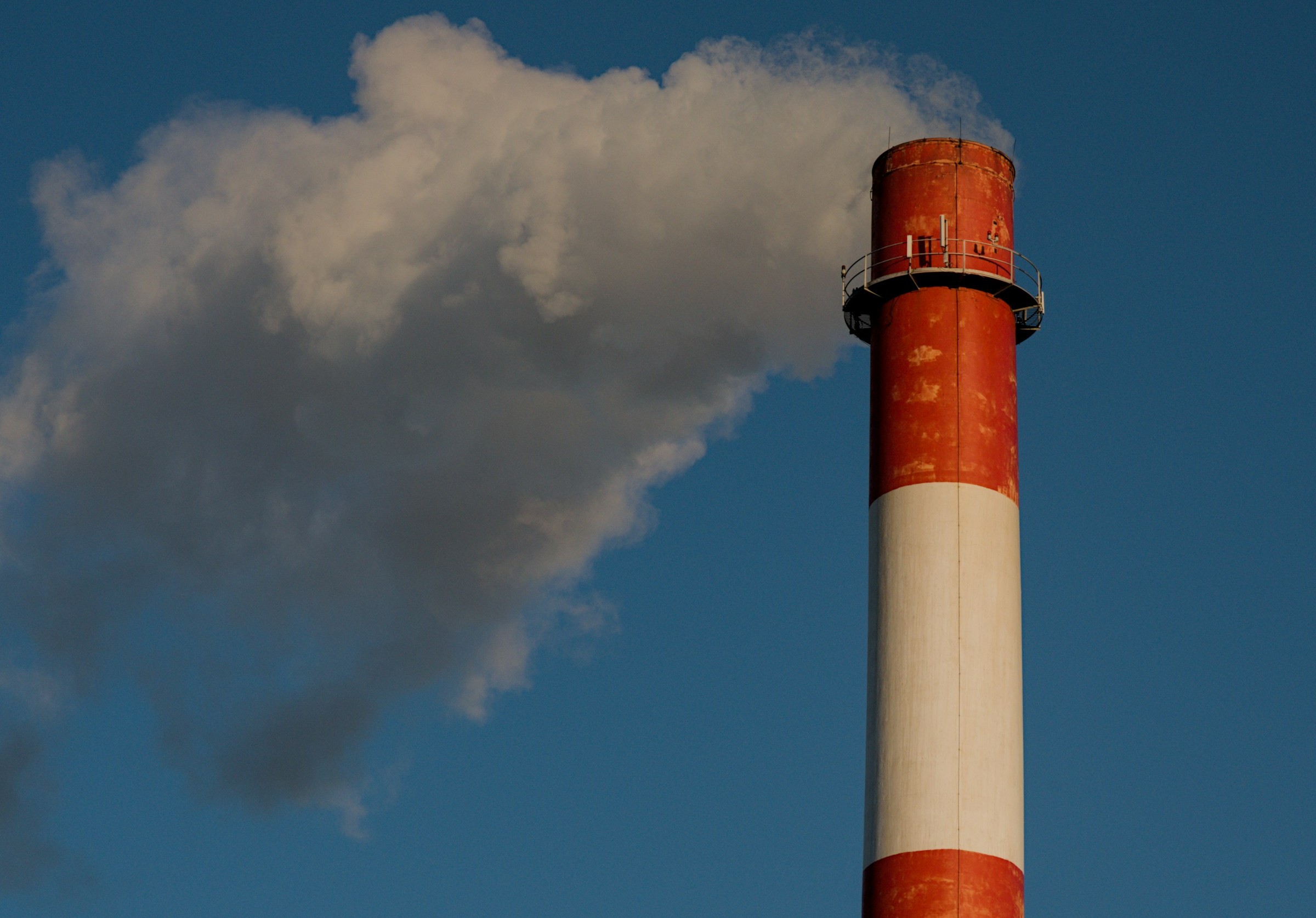 A close-up shot capturing a tall industrial chimney stack releasing a plume of smoke against a clear blue sky