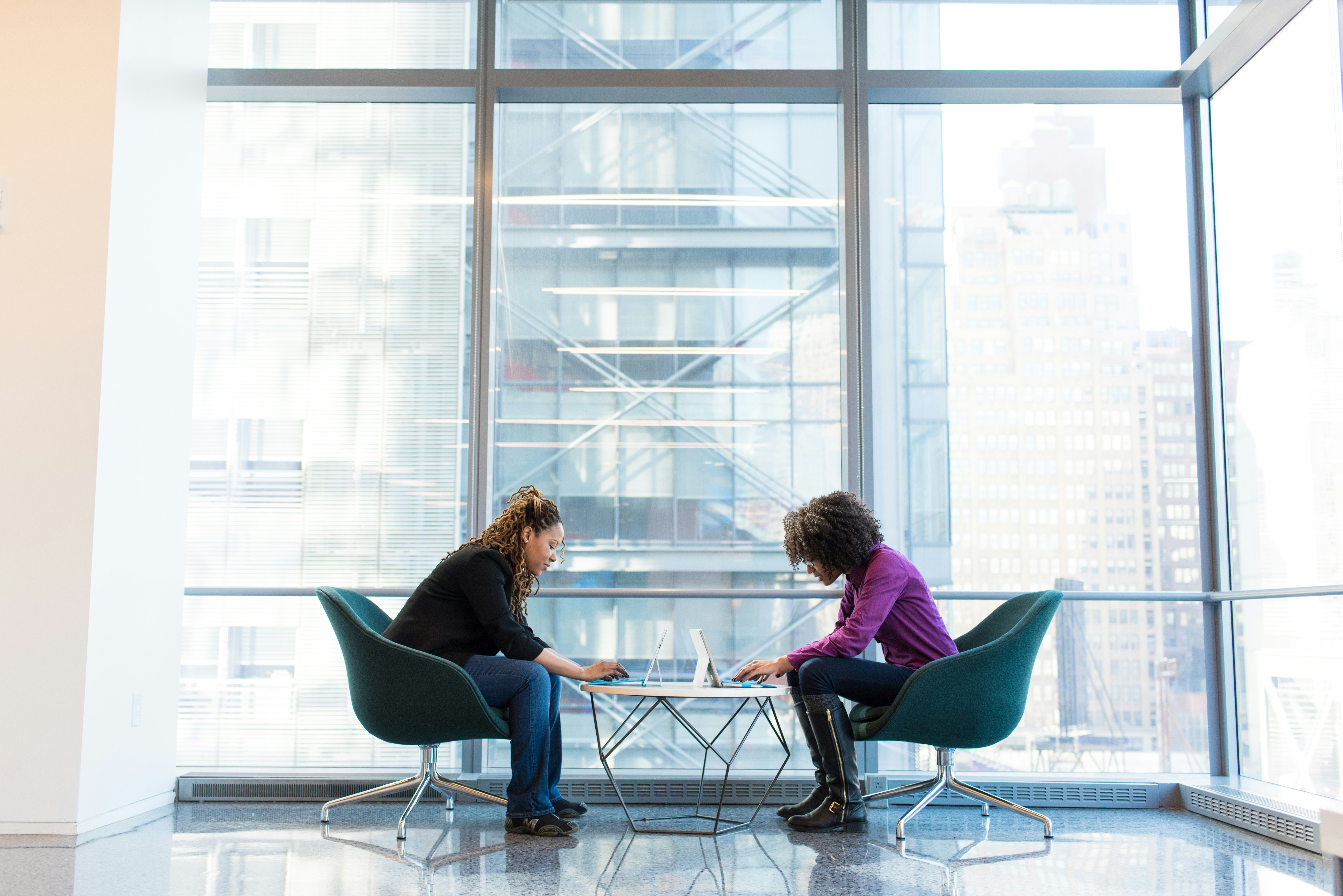 This image shows two individuals collaborating with laptops at a modern office table