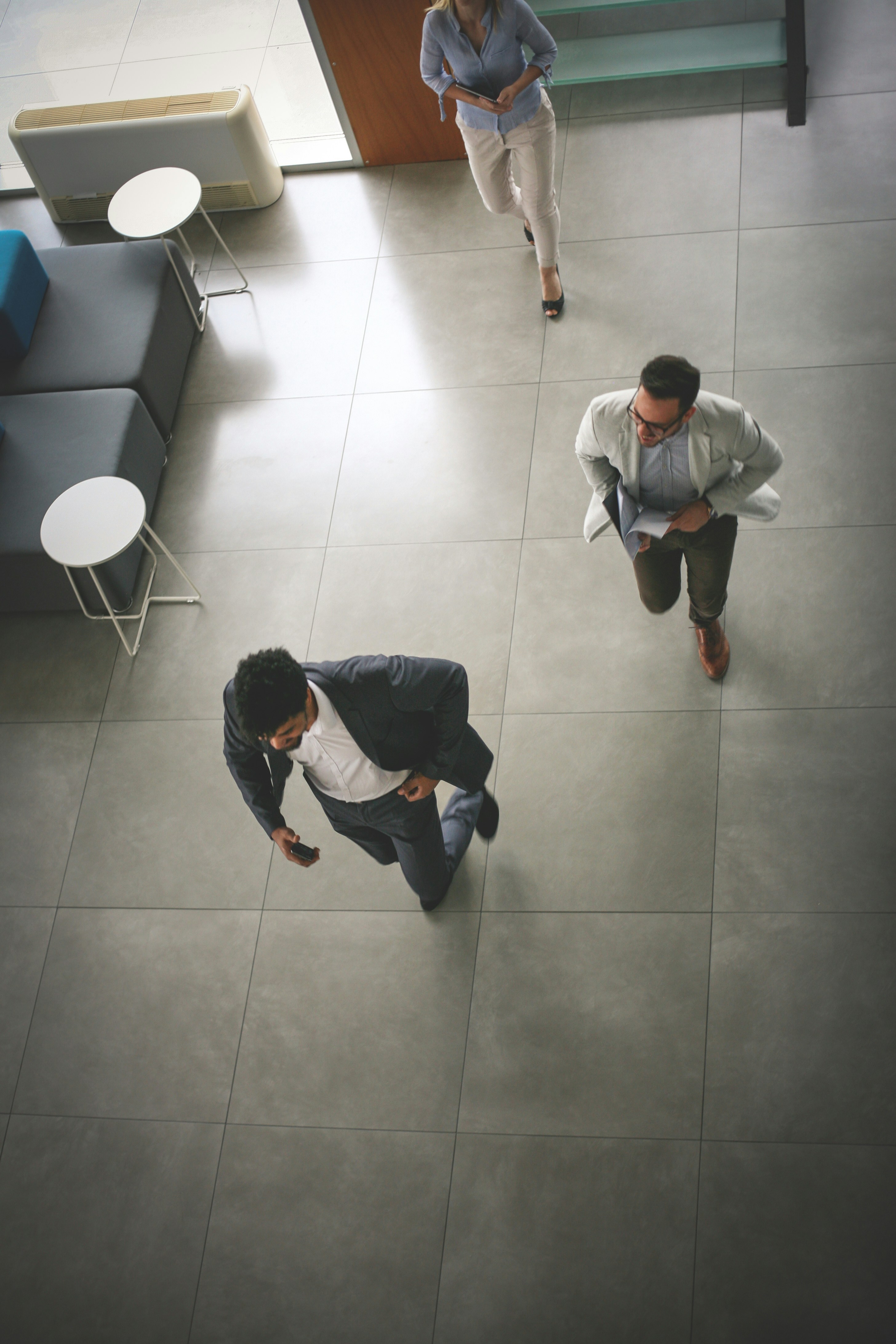 The image appears to show three business professionals moving quickly through a bright office lobby