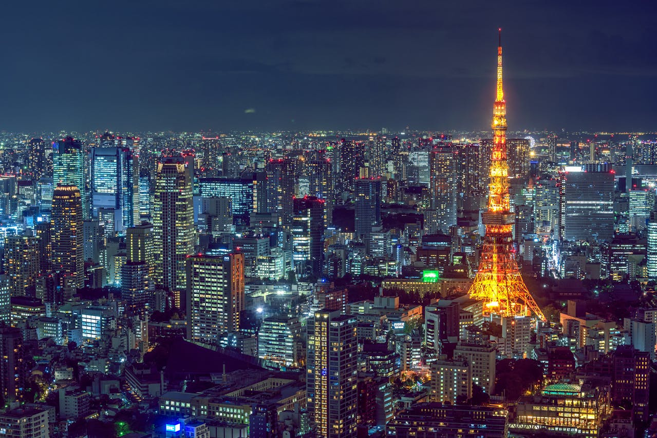 An elevated, wide-angle night view capturing the brightly lit cityscape of Tokyo, Japan, dominated by Tokyo Tower