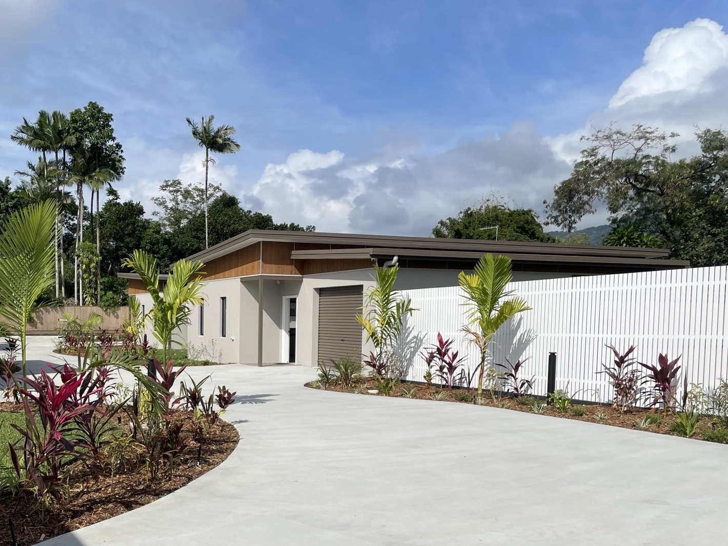 Contemporary unit complex with landscaped garden beds, concrete paths, and mountain views in the background."