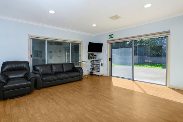 Spacious lounge room with black leather sofas, mounted television, and large glass sliding doors opening to the outside.