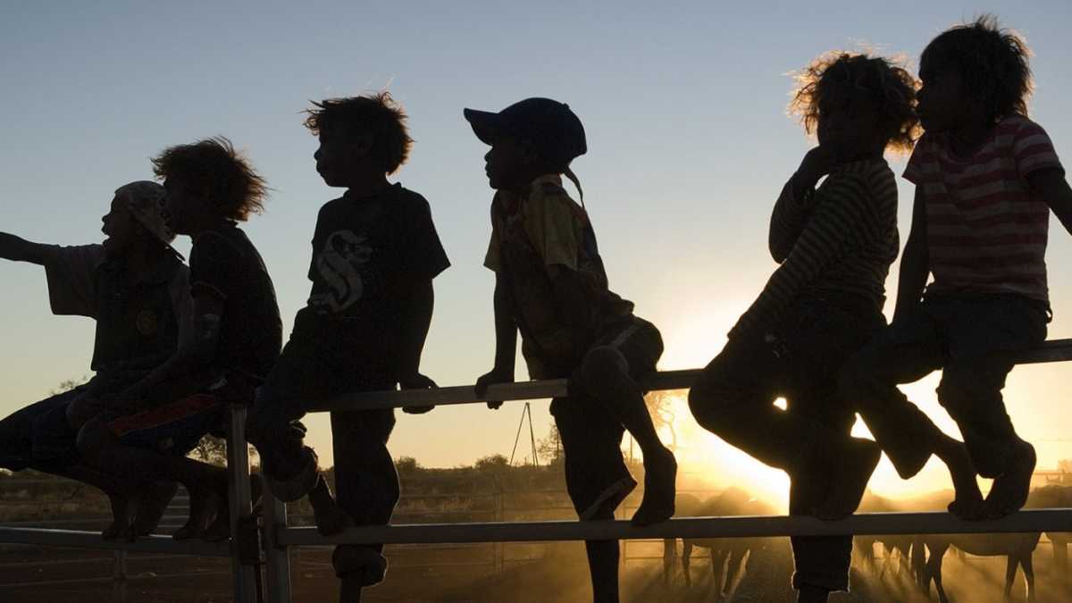 Silhouette of Indigenous children sitting on a fence.