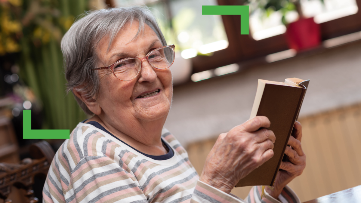 older women wearing a striped shirt reading a brown book.