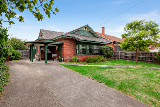 --Front of brick home with a lawn, driveway and trees.--