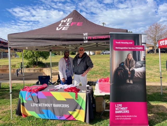 Darelle Brown, Case Manager, and Jack Dempsey, Program Manager, standing behind the Life Without Barriers booth, smiling at the camera.