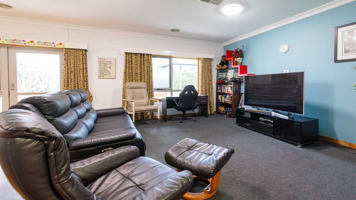 Grey couch, armchairs, facing large television, large windows.