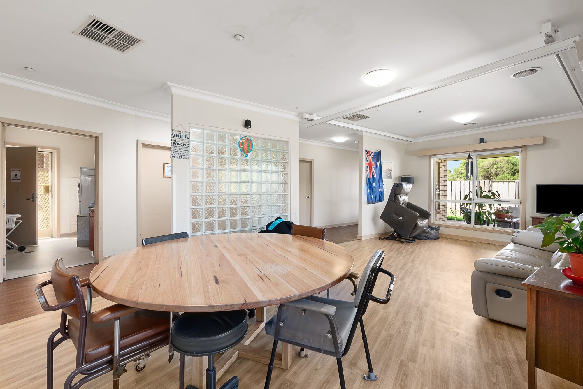 Spacious open-plan room with round wooden table, recliners, and large window.