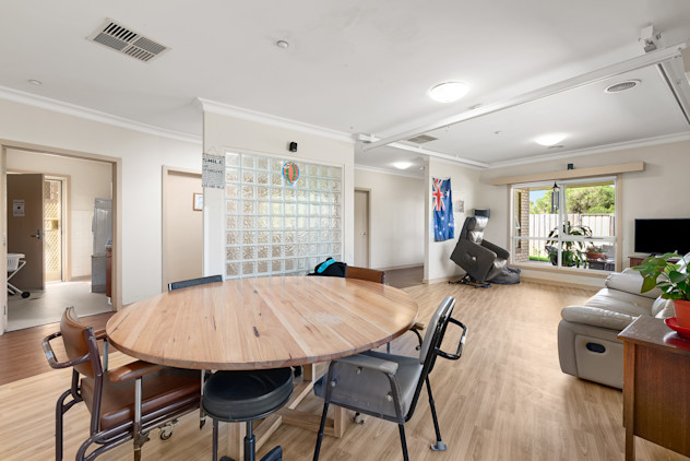 Spacious open-plan room with round wooden table, recliners, and large window.