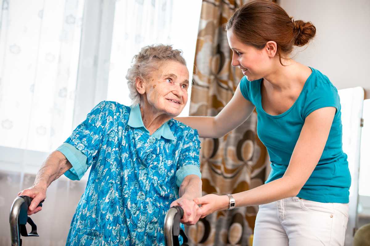 An older woman with a walking frame smiling at a friendly support worker.
