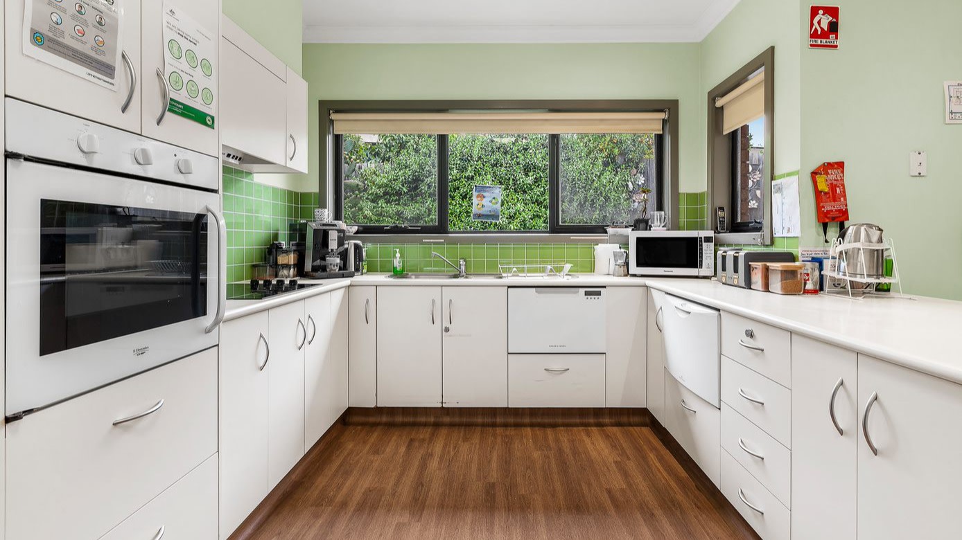 --A U-shaped kitchen with white cabinets and benches, green tiling, an oven, stove and microwave.--