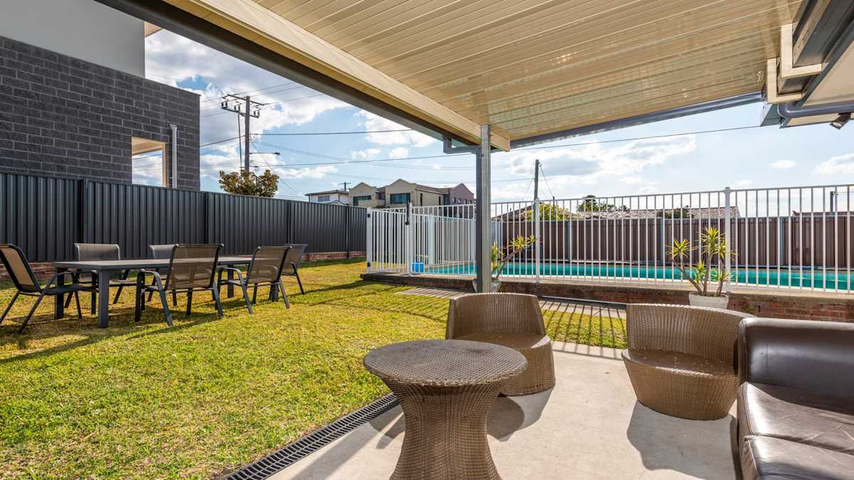 Spacious fully fenced lawned area out back with large inground pool, security fence, undercover patio with couches and chairs.