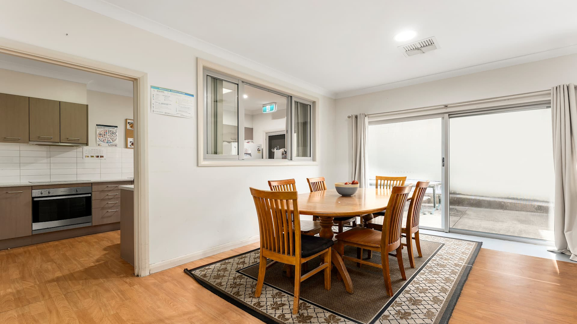 wooden dining table on floor rug near sliding door exit to back area.