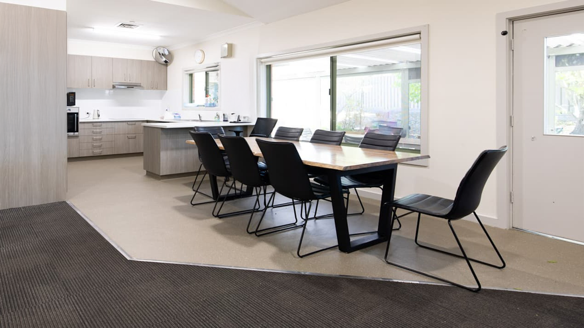 Kitchen overlooks dining table and chairs on hard flooring with windows and door opening to backyard.