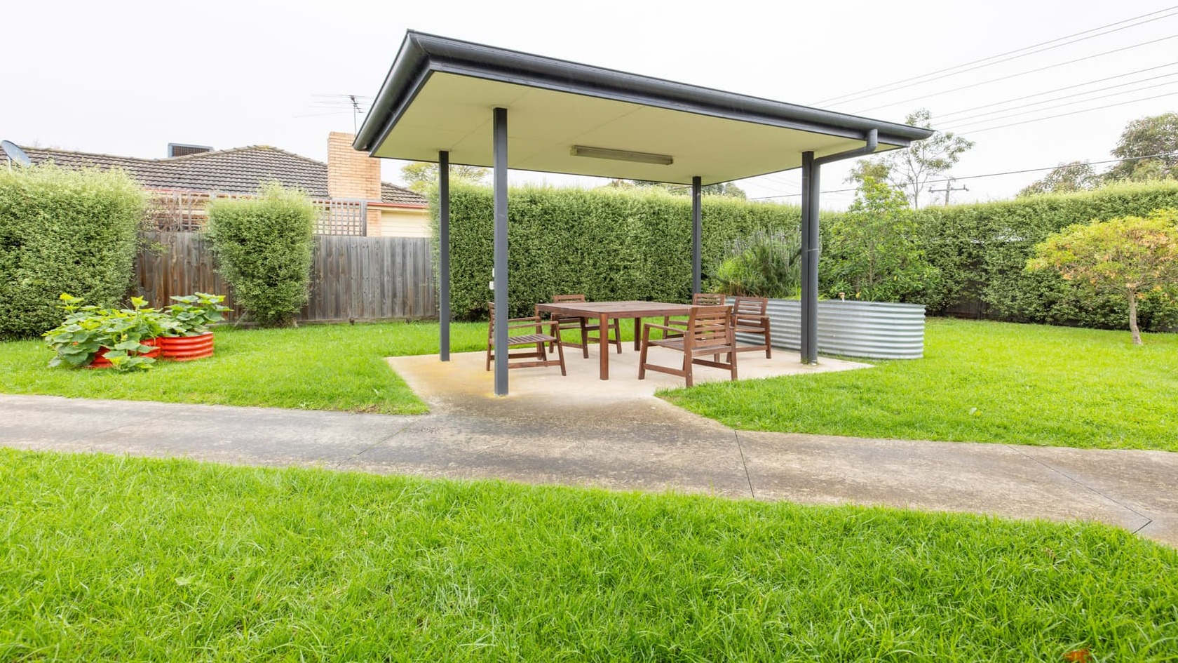 Spacious lawned area with wide concrete walkways, leading to a centrally located covered pergola with table and chairs.