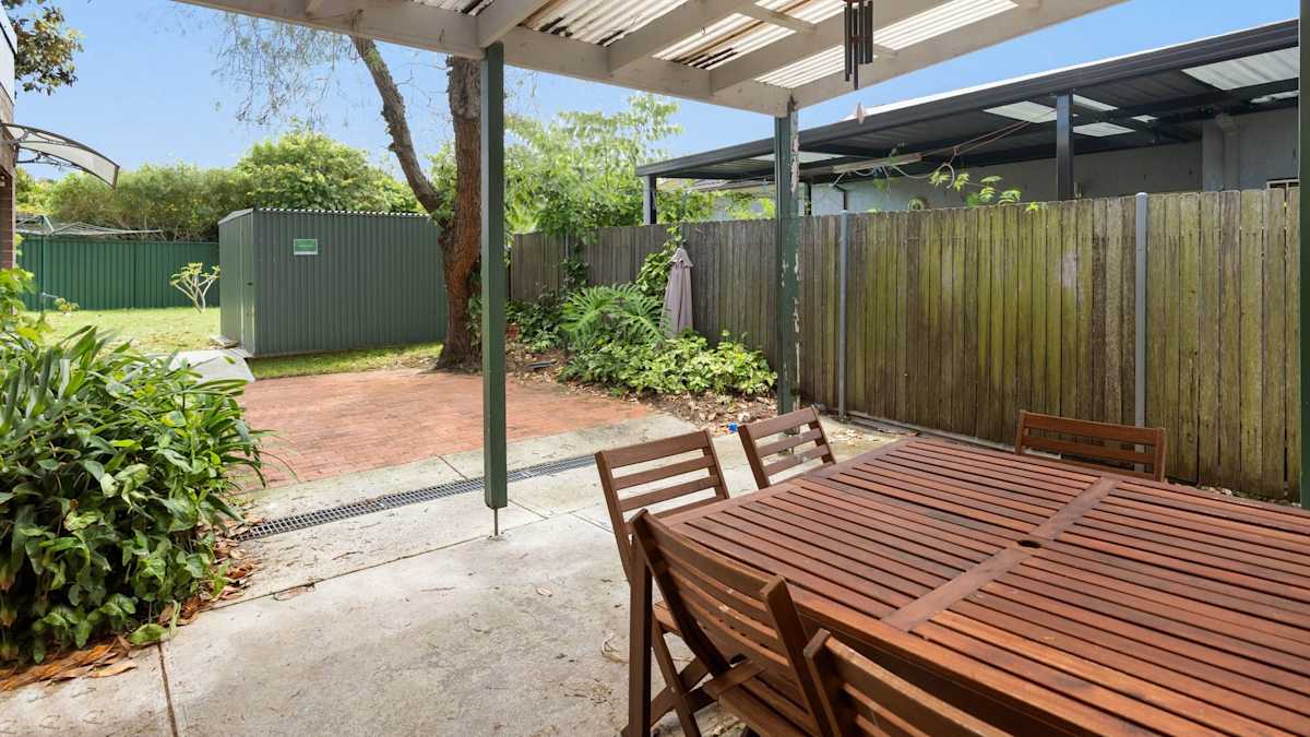Undercover patio with outdoor, wooden setting overlooking lawn and gardens.