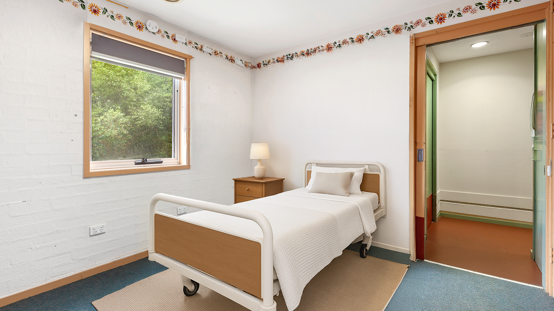 blue hard floor, large window, flower mural running along the tops of the wall, white chest of drawers and artwork on the walls.