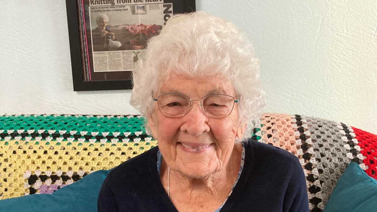 Betty sits on her couch in her home in front of a photo frame.