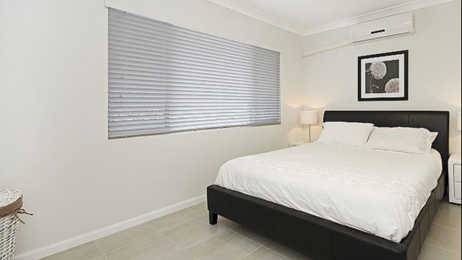 White tiled bedroom with air conditioning and a queen bed. 