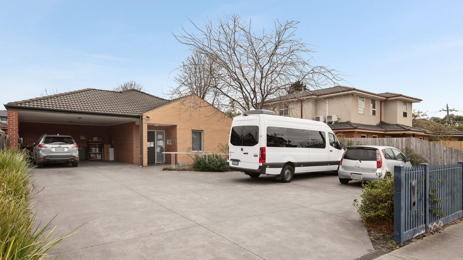 --Front of Oakleigh South house with concrete driveway leading to a carport. Three cars are parked in the driveway.--