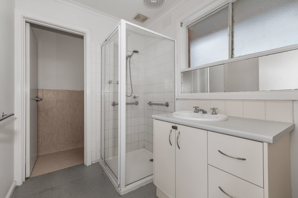 --Bathroom with sink, cabinets, mirror and shower. The shower has handrails inside.--
