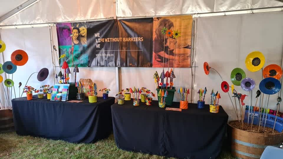 Inside a white marquee with two tables set up with colourful ceramic garden art in front of a Life Without Barriers sign.