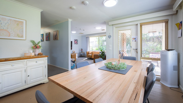 Dining space with wooden table and black chairs, decorated sideboard, and view into living room.